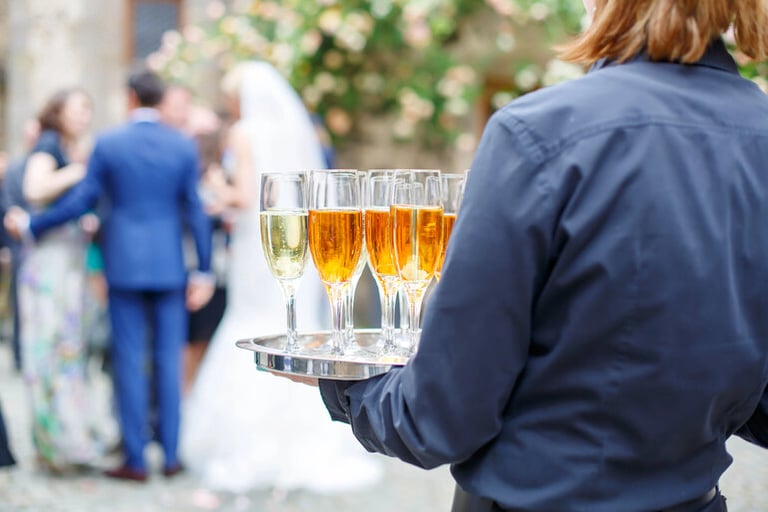 A waiter holding a tray of beer and champagne at a wedding reception with guests and a bride in the background