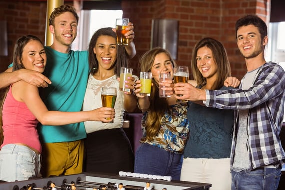 Group of friends playing poker and celebrating in a lively bar setting with drinks and poker chips on the table.