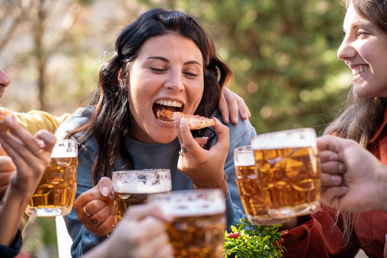 Friends enjoying themselves in a social setting, drinking beer, and laughing together while sharing food.