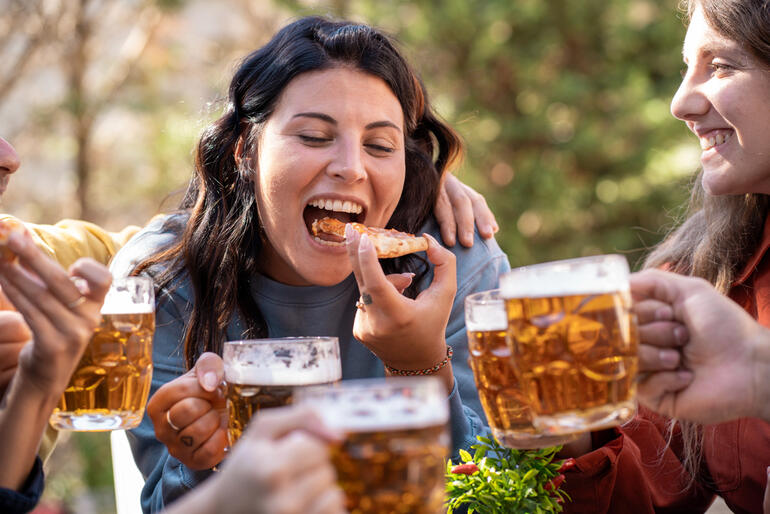 Friends enjoying themselves in a social setting, drinking beer, and laughing together while sharing food.