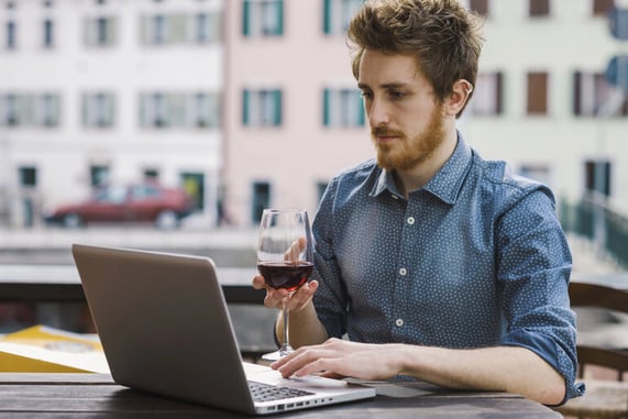 Man using a laptop while holding a glass of beer outdoors, reflecting online gaming comparison for beer lovers.
