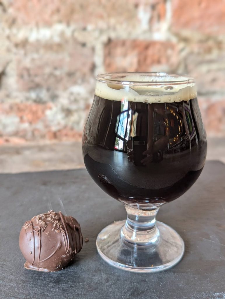 A tulip glass of imperial stout on a table next to an oreo cream cheese truffle
