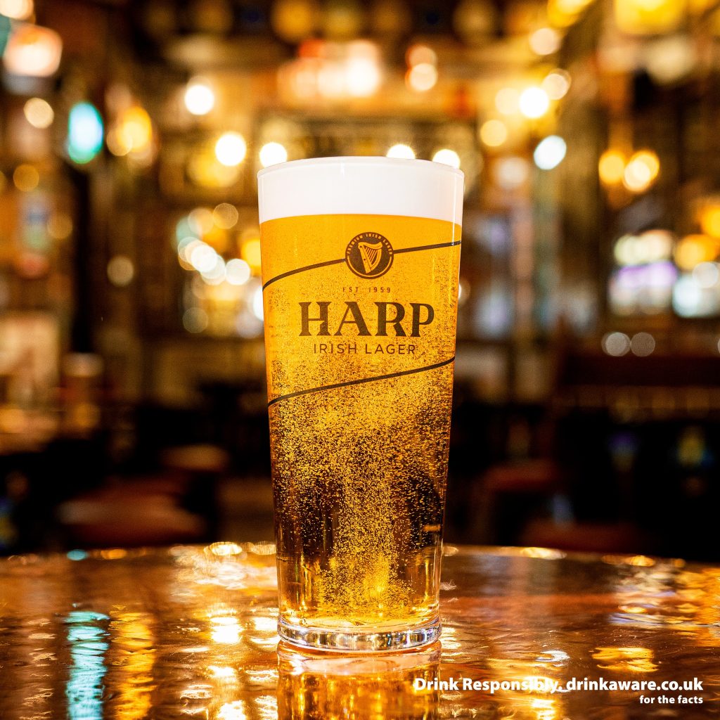 Glass of Guinness Harp lager on a a shiny table in a warmly lit bar