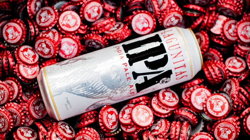 A super tall boy can of Laguanitas IPA sitting on a bed of bottle caps.