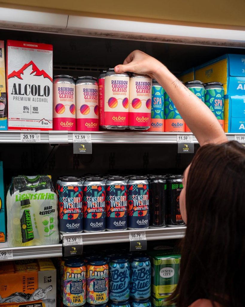Woman grabbing four pack of tall-boy cans from grocery store shelf