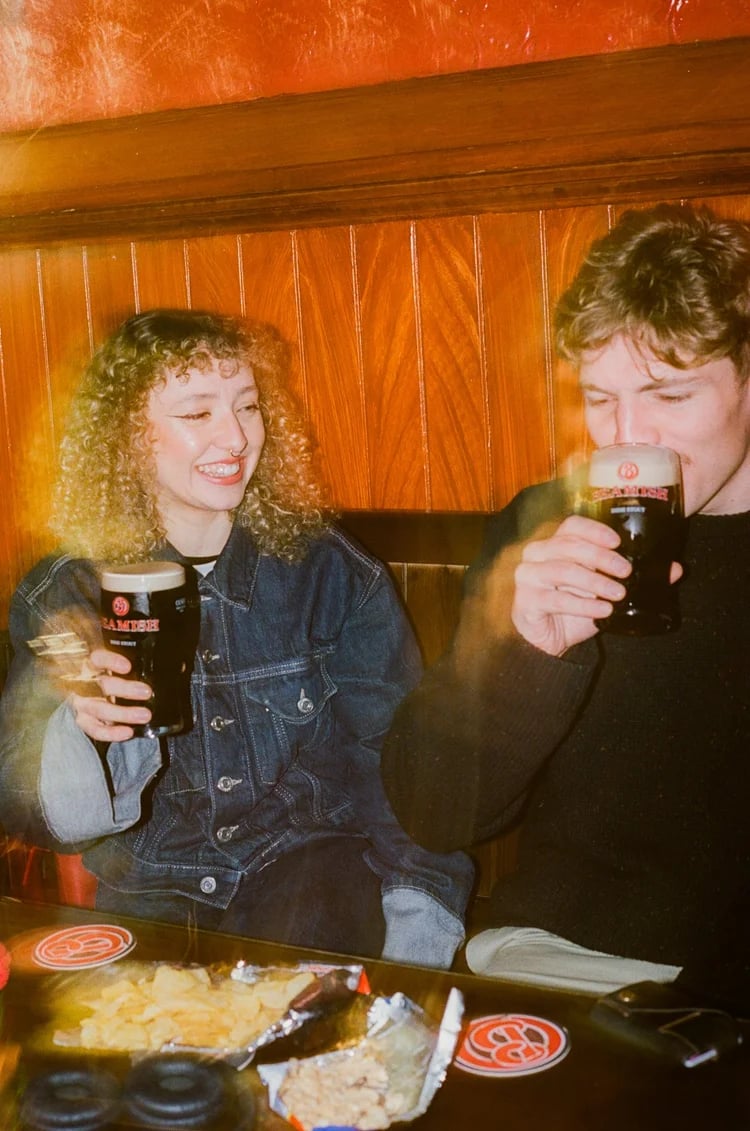 A girl and a boy sitting while having a glass of Beamish Irish Stout
