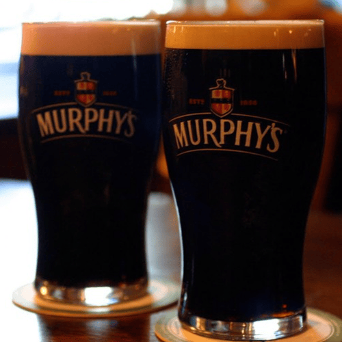 Two glasses of Murphy’s Irish Stout are placed on a wooden table with a Murphy's lable on them