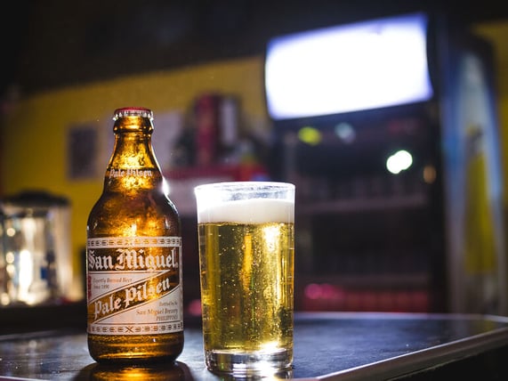 San Miguel Pale Pilsen bottle and glass of beer on a bar counter with warm ambient lighting.