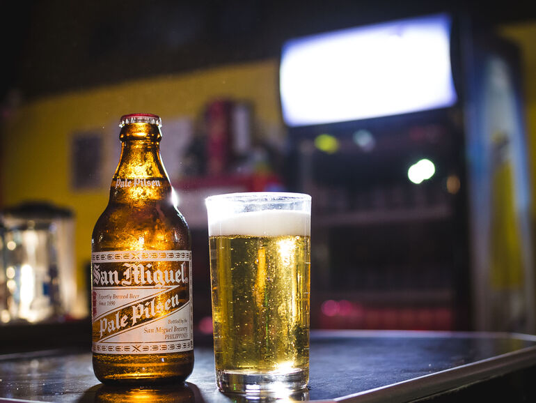 San Miguel Pale Pilsen bottle and glass of beer on a bar counter with warm ambient lighting.